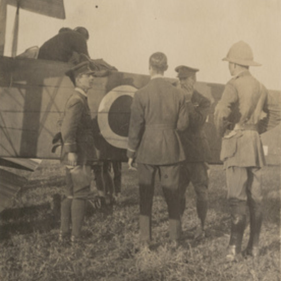 Image: men standing around the tail of a biplane.