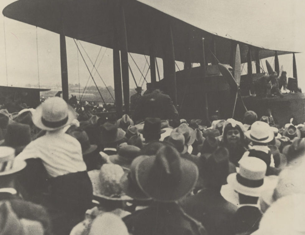 Large biplane surrounded by crowds of people.