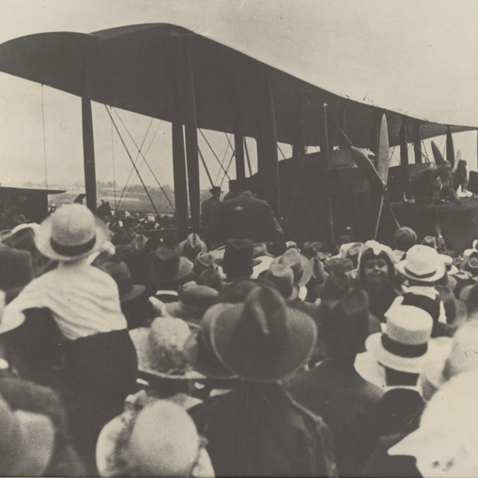 Large biplane surrounded by crowds of people.