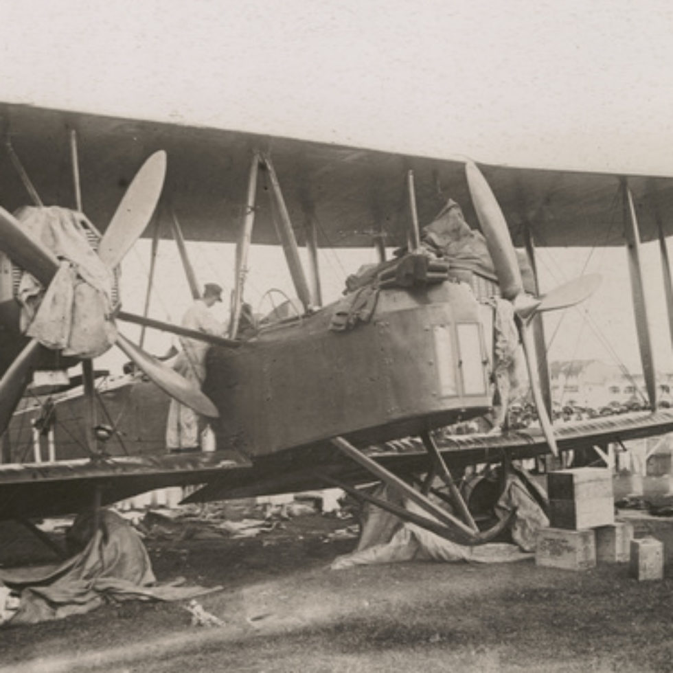 Image: Close up of Biplane with rags covering wheels and the engines. One of the crew is looking into the cockpit from the wing.