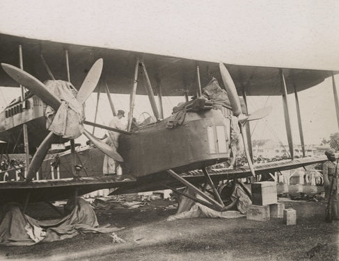 Image: Close up of Biplane with rags covering wheels and the engines. One of the crew is looking into the cockpit from the wing.